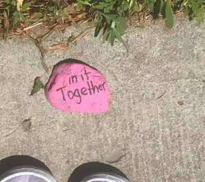 Pink stone on sidewalk, painted to read "in it together."