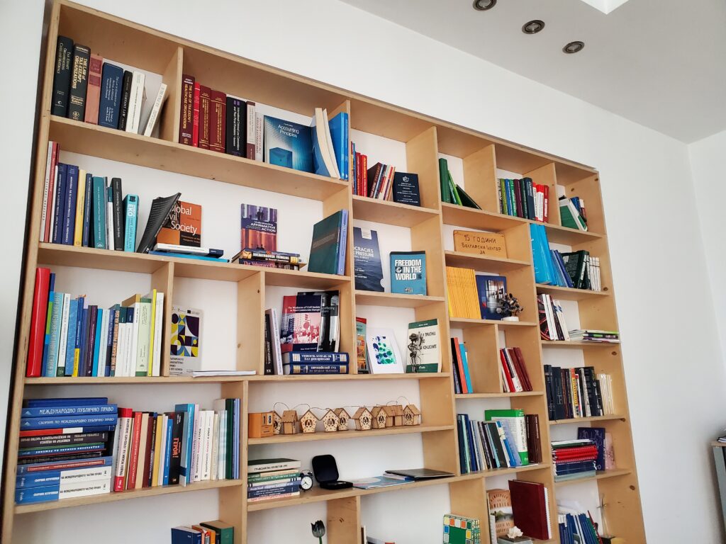 The bookshelf in the BCNL office: a tall, open wooden shelf with a range of books in English and Bulgarian.